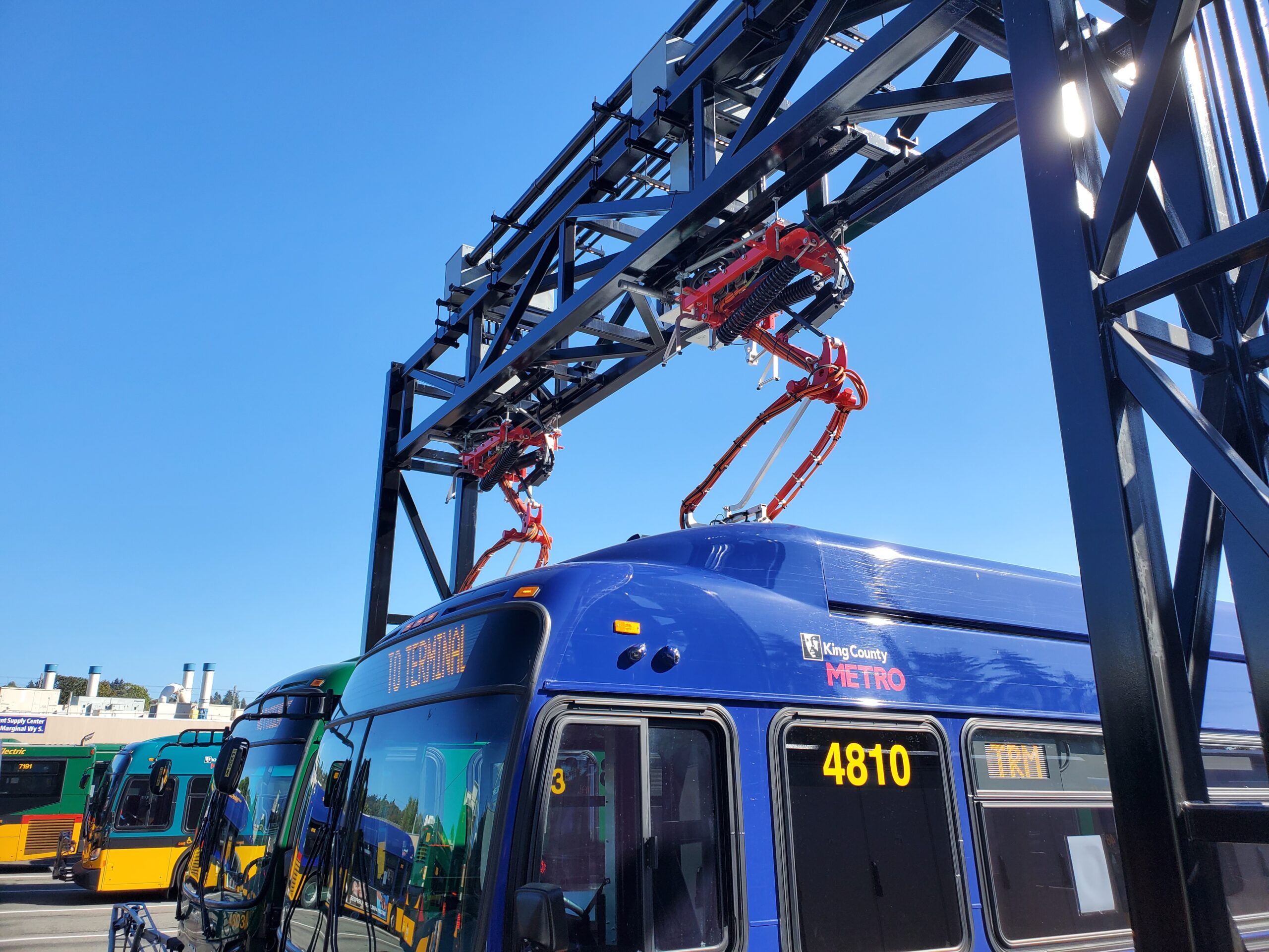 Picture of an overhead pantograph charger extending from overhead structure onto bus rooftop